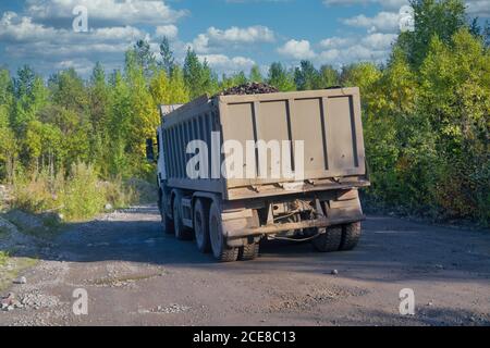 Un camion-benne se déplace sur une route de terre sur le fond de la forêt et du ciel bleu d'été. Banque D'Images