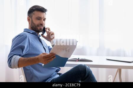 Appel professionnel. Beau jeune homme d'affaires qui vérifie les rapports financiers et parle au téléphone portable Banque D'Images