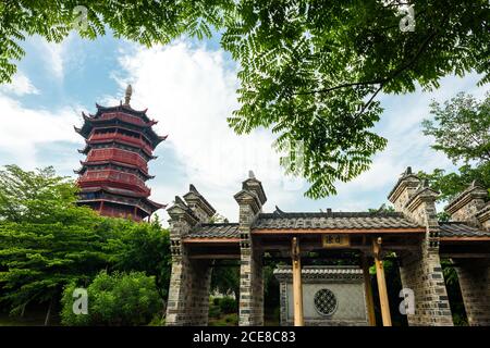 Vue pittoresque à angle bas de beau bâtiment ornemental de traditionnel Pagode chinoise encadrée par des branches d'arbre vertes contre le bleu nuageux Ciel en été à Xiamen en Chine Banque D'Images