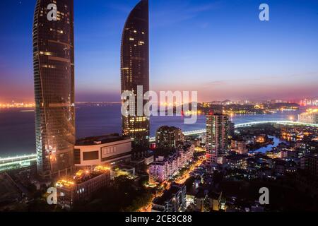 D'en haut, vue magnifique sur les rues illuminées du quartier moderne De la ville côtière de Xiamen en Chine avec des gratte-ciels contemporains contre ciel coloré le soir Banque D'Images