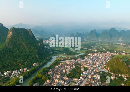 Vue de drone avec des maisons résidentielles situées dans la vallée et entouré de roches vertes dans le comté de Yangshuo, en Chine Banque D'Images