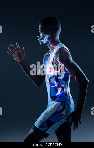 Vue latérale d'un sportif afro-américain sérieux et sportif en couleurs active wear pour des mouvements rapides en studio sombre avec éclairage au néon rouge Banque D'Images