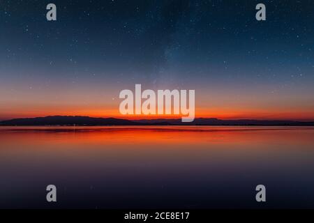 Ciel étoilé au crépuscule sur la mer calme avec le horizon au milieu et les montagnes en arrière-plan Banque D'Images