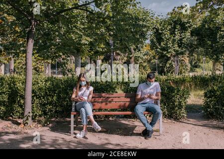 Couple au parc en utilisant le smartphone, portant des masques et respectant les distances sociales pendant une pandémie Banque D'Images