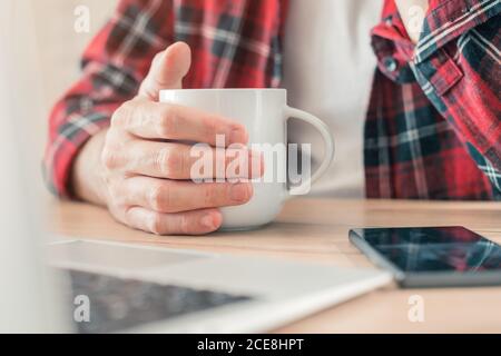 Café du matin dans un bureau indépendant à domicile, gros plan de la main avec une tasse, mise au point sélective Banque D'Images