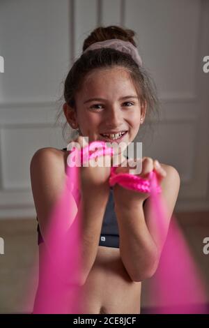 Bonne adolescente en noir sportswear s'échauffe avec du rose bande élastique souriant à l'appareil photo Banque D'Images