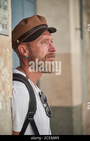 Vue latérale d'un randonneur à barbe adulte dans une tenue tendance et une casquette avec des accessoires élégants et un sac à dos qui vous permettent de vous éloigner de l'extérieur Banque D'Images