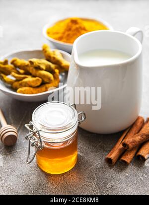 Ingrédients pour le Latte curcuma. Curcuma moulu, racine de curcuma, cannelle, pot de lait sur fond de béton gris. Vue de dessus, espace de copie Banque D'Images