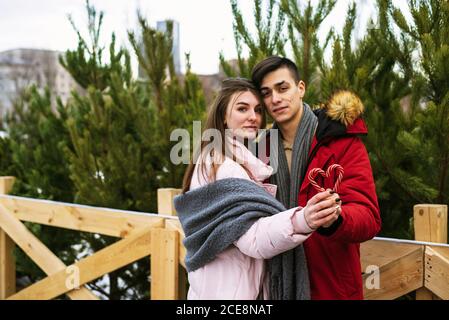 Un jeune couple tient une canne en sucre en forme de coeur et enserre. Portrait urbain des amoureux. Concept Noël, nouvel an et amour. Extérieur. Banque D'Images