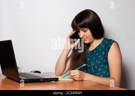 Une femme de 25 ans parle au téléphone et prend des notes dans un ordinateur portable. Travail de bureau Banque D'Images