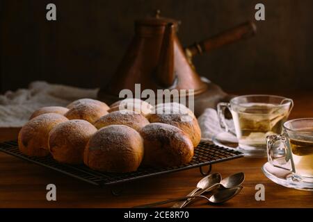 Pains appétissants identiques de forme ronde et de surface dorée avec de la poudre de sucre sur une grille de refroidissement en métal sur une table en bois Banque D'Images