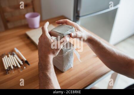 ceramiste mâle méconnaissable assis à la table et préparant l'argile pour création de poteries Banque D'Images