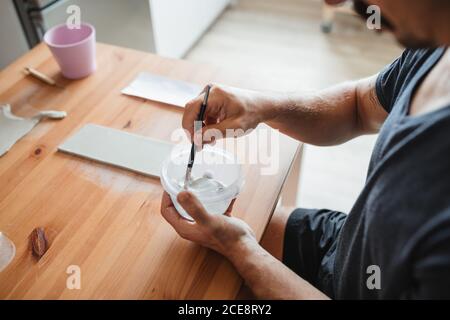 Vue du dessus du côté de la récolte mâle céramiste assis à table et mélange du liquide dans un bol pour travailler dans les modernes atelier Banque D'Images