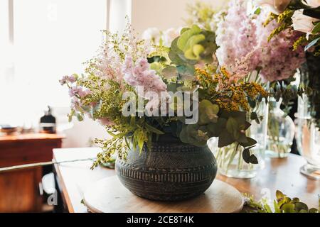 Beau bouquet de fleurs diverses dont des fleurs de craspedia avec du vert branches d'eucalyptus disposées en pot en céramique ornementale placé sur la table en studio de fleuriste créatif Banque D'Images