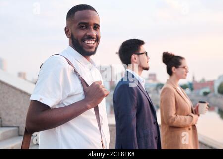 Portrait d'étudiant noir gai avec la poignée de maintien de la barbe porte-documents debout dans une ligne de contraintes de groupe Banque D'Images