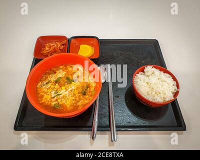 Ramyeon, plat coréen de nouilles instantanées. Rouge et épicé, avec des œufs, des oignons verts hachés et des piments. Kimchi et un bol de riz blanc. Banque D'Images