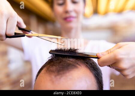 Rognez le coiffeur souriant dans le t-shirt à l'aide du peigne en plastique et ciseaux tout en coupant les cheveux à homme sans visage dans le salon de coiffure Banque D'Images