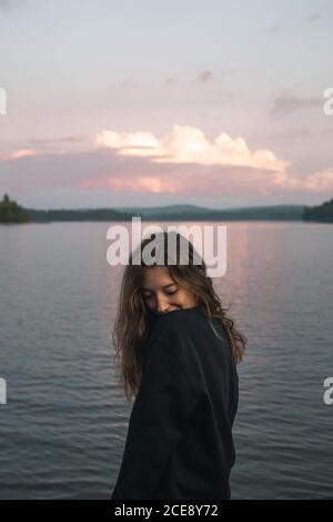 Vue latérale d'une femme de voyage sereine se tenant près du lac à l'intérieur Parc provincial Algonquin lors d'un incroyable coucher de soleil Banque D'Images