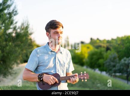 Photo de foyer peu profond d'un jeune homme caucasien jouant ukulele dans le parc Banque D'Images