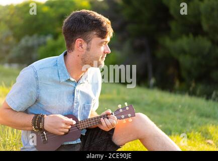 Photo de foyer peu profond d'un jeune homme caucasien jouant ukulele dans le parc Banque D'Images