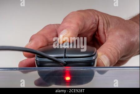 Gros plan de la main d’un homme à l’aide d’une souris d’ordinateur (périphérique d’entrée), avec molette de défilement, en gris / gris, sur une surface transparente. Banque D'Images