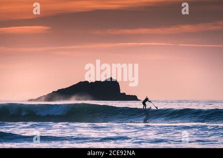 Une paddle Boarder pagayer près de Goose Rock silhouetted par la lumière de la fin de soirée à Fistral à Newquay, en Cornouailles. Banque D'Images