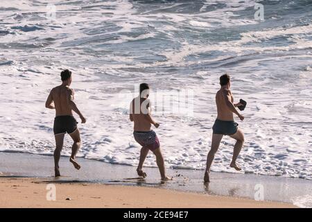 Trois amis mâles qui se sont exécutés dans la mer à Fistral Beach à Newquay, en Cornouailles. Banque D'Images