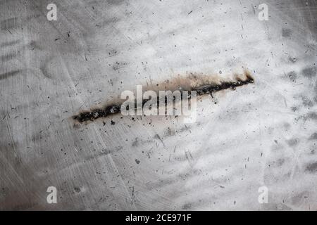 Un cordon de soudure droit noir sur une plaque métallique argentée brillante avec des traces de fumée et de scories. Banque D'Images
