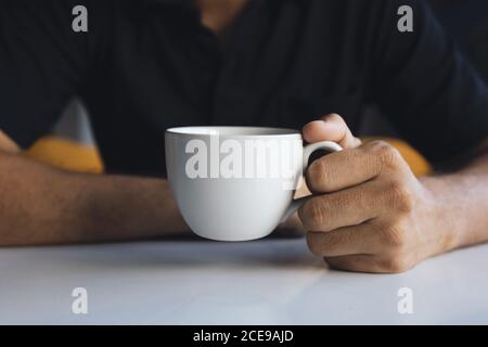 gros plan main d'un homme d'affaires tenant une tasse blanche de café dans la pièce avec une mise au point douce et une lumière excessive l'arrière-plan Banque D'Images