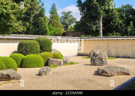 Jardin zen japonais avec galets ratifiés, arbustes taillés avec soin, pierres ornementales et mur environnant Banque D'Images