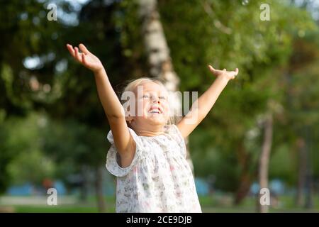 Mignonne Siling Little Blond Girl avec des bras ouverts levés dans le parc ayant l'amusement. Banque D'Images