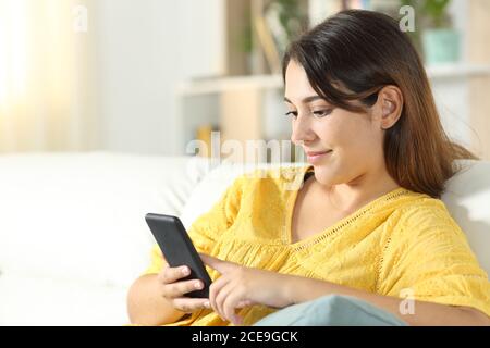 Fille en jaune utilisant un téléphone portable assis sur un canapé dans le salon à la maison Banque D'Images