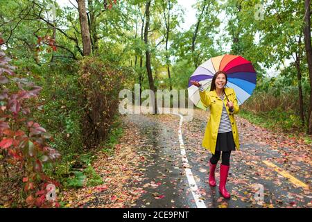 Femme asiatique d'automne heureuse après la pluie marchant avec un parapluie. Mannequin regardant vers le ciel clair joyeuse le jour de l'automne pluvieux portant un imperméable jaune Banque D'Images