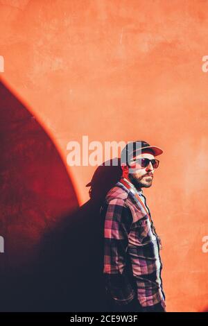 Portrait d'un homme barbu élégant posé sur un mur rouge ensoleillé. CopySpace. Banque D'Images