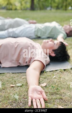 Gros plan d'une femme calme allongé avec les bras étirés sur l'herbe et se détendre dans le shavasana après la pratique du yoga Banque D'Images