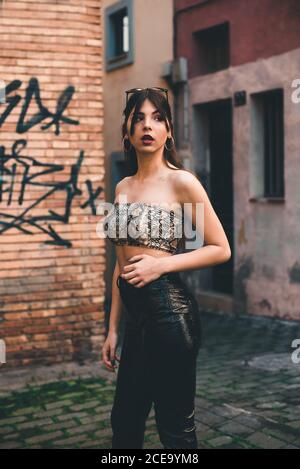 Jeune femme en cuir noir pantalon or anneaux et lunettes de soleil sur la tête en restant à l'écart de la rue Banque D'Images