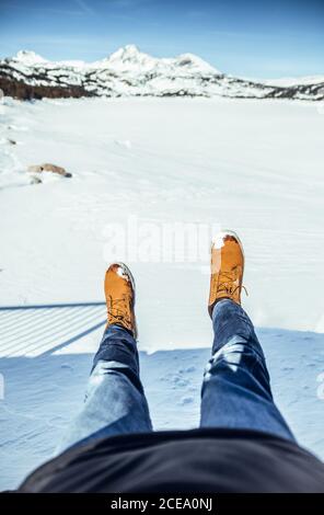 Rognez les jambes des hommes en jeans et en bottes d'hiver, assis sur la neige par temps ensoleillé, près des collines de Cerdanya, en France Banque D'Images