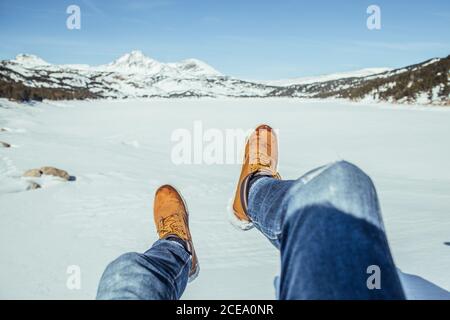 Rognez les jambes des hommes en jeans et en bottes d'hiver, assis sur la neige par temps ensoleillé, près des collines de Cerdanya, en France Banque D'Images