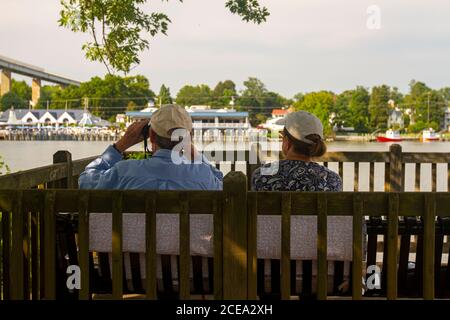 Un couple âgé portant des chapeaux de baseball est assis sur un banc extérieur en bois dans une terrasse de jardin près du Chesapeake et du canal du Delaware. L'homme âgé est Banque D'Images