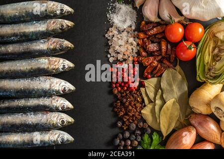 Ensemble d'épices diverses à proximité de crevettes fraîches et d'anchois sur fond noir Banque D'Images
