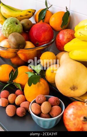 Collection de différents fruits tropicaux mûrs savoureux frais dans des bols et des assiettes sur la table près de wall Banque D'Images