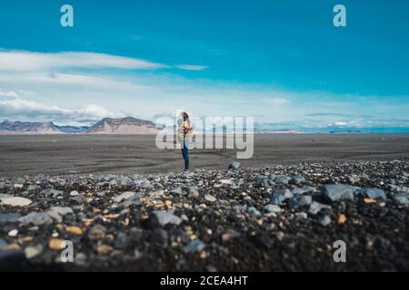 Vue latérale d'une jeune femme se tenant dans une campagne étonnante et profitant de la vue tout en voyageant à travers l'Islande Banque D'Images