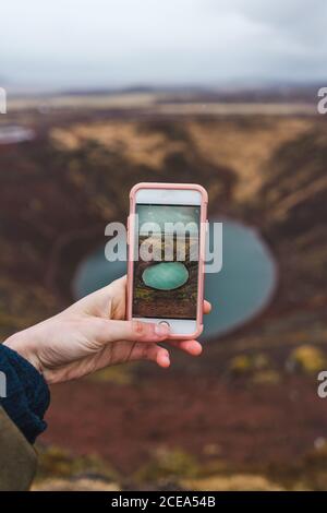 Rognez la main de la femme tenant un smartphone et prenant la photo du petit lac au fond de la fosse ouverte. Banque D'Images