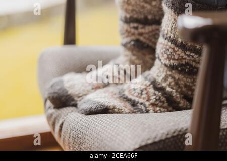 Crop jambes de femme dans doux chaussettes chaudes debout sur un fauteuil confortable dans la chambre confortable Banque D'Images