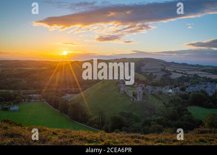 Lever du soleil avec un coucher de soleil sur la campagne du Dorset avec le château de Corfe et les collines illuminées du soleil du matin. Banque D'Images