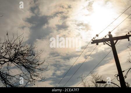 Silhouette fils et arbres de téléphone avec le soleil derrière un Ciel nuageux en arrière-plan Banque D'Images