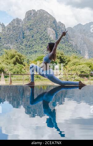 Vue latérale d'une jeune femme qui s'étire et médite à la piscine dans la nature. Banque D'Images