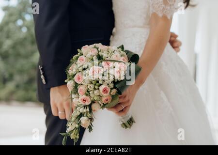 Vue de côté rognée de la mariée tenant un bouquet rose et baiser avec le marié à l'extérieur Banque D'Images