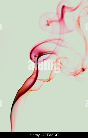 Les boucles de fumée rouge fin swirling sur fond vert clair Banque D'Images