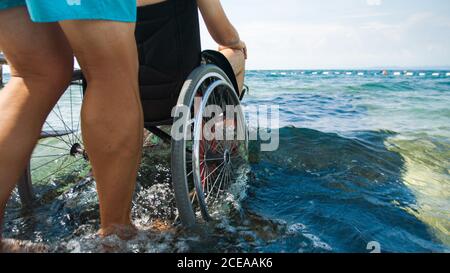 Homme handicapé à la plage nageant sur un fauteuil roulant avec aide sur une rampe d'accès. Banque D'Images